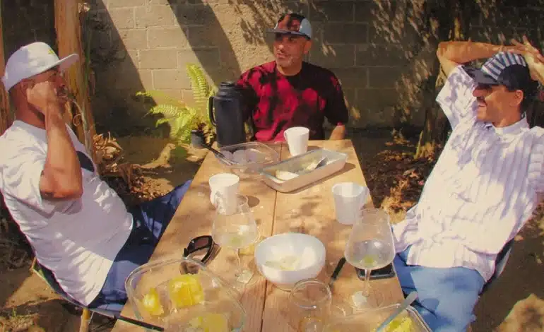 foto mostra os membros do grupo Conteúdo Paralelo sentados próximos a uma mesa em um quintal, tomando café da tarde